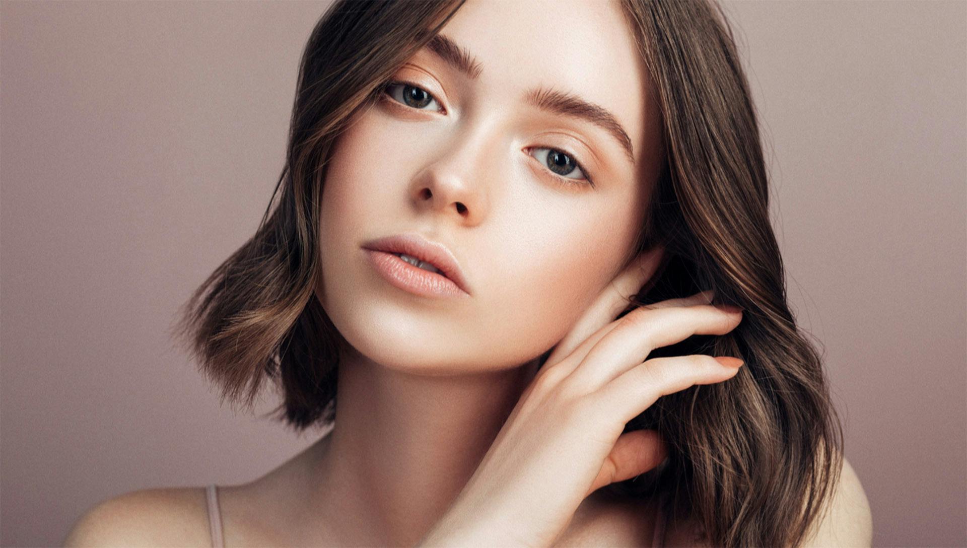 Woman with clear skin looking forward, hand next to her face