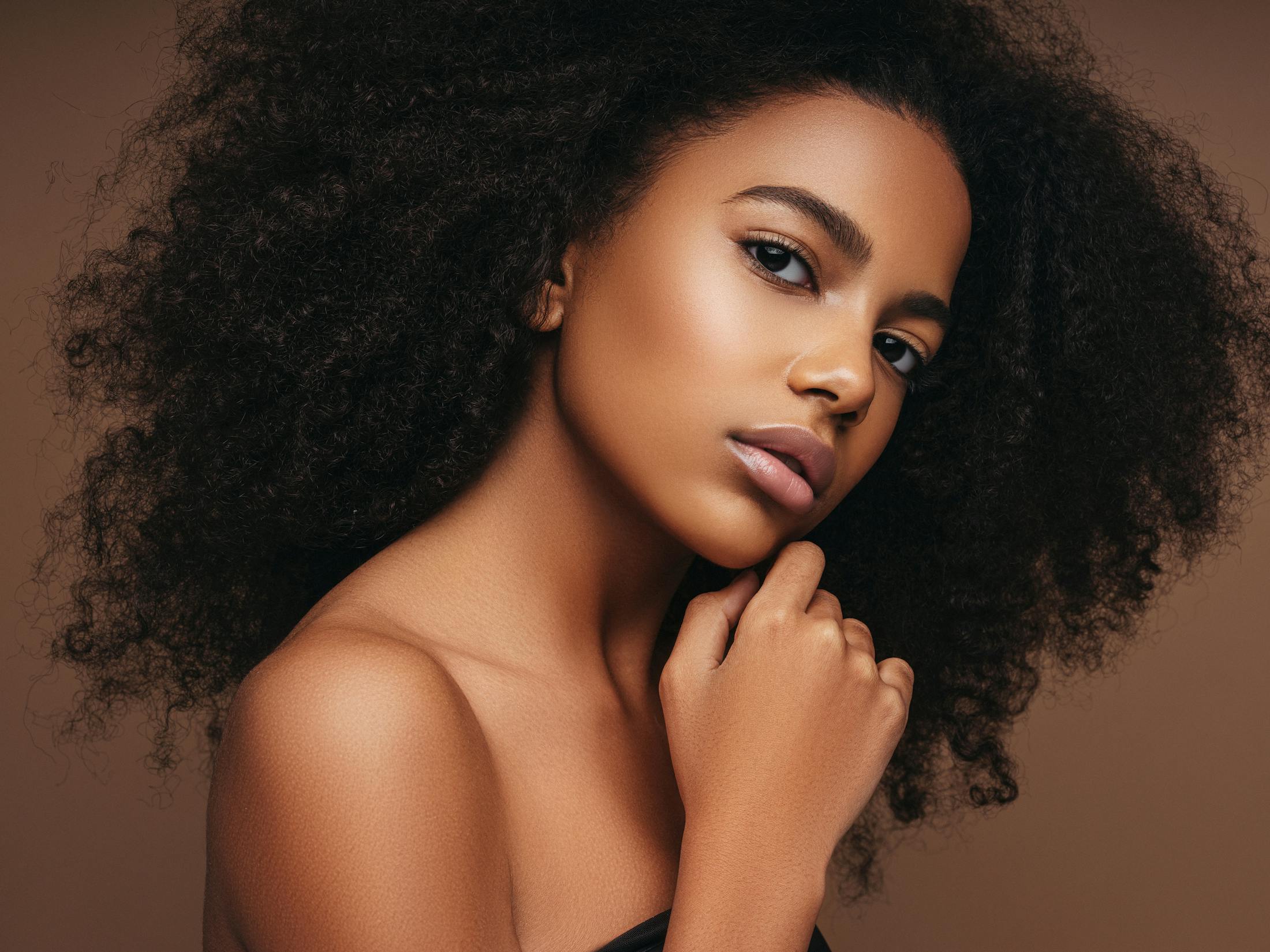 A woman with curly hair posing with hand to her chin