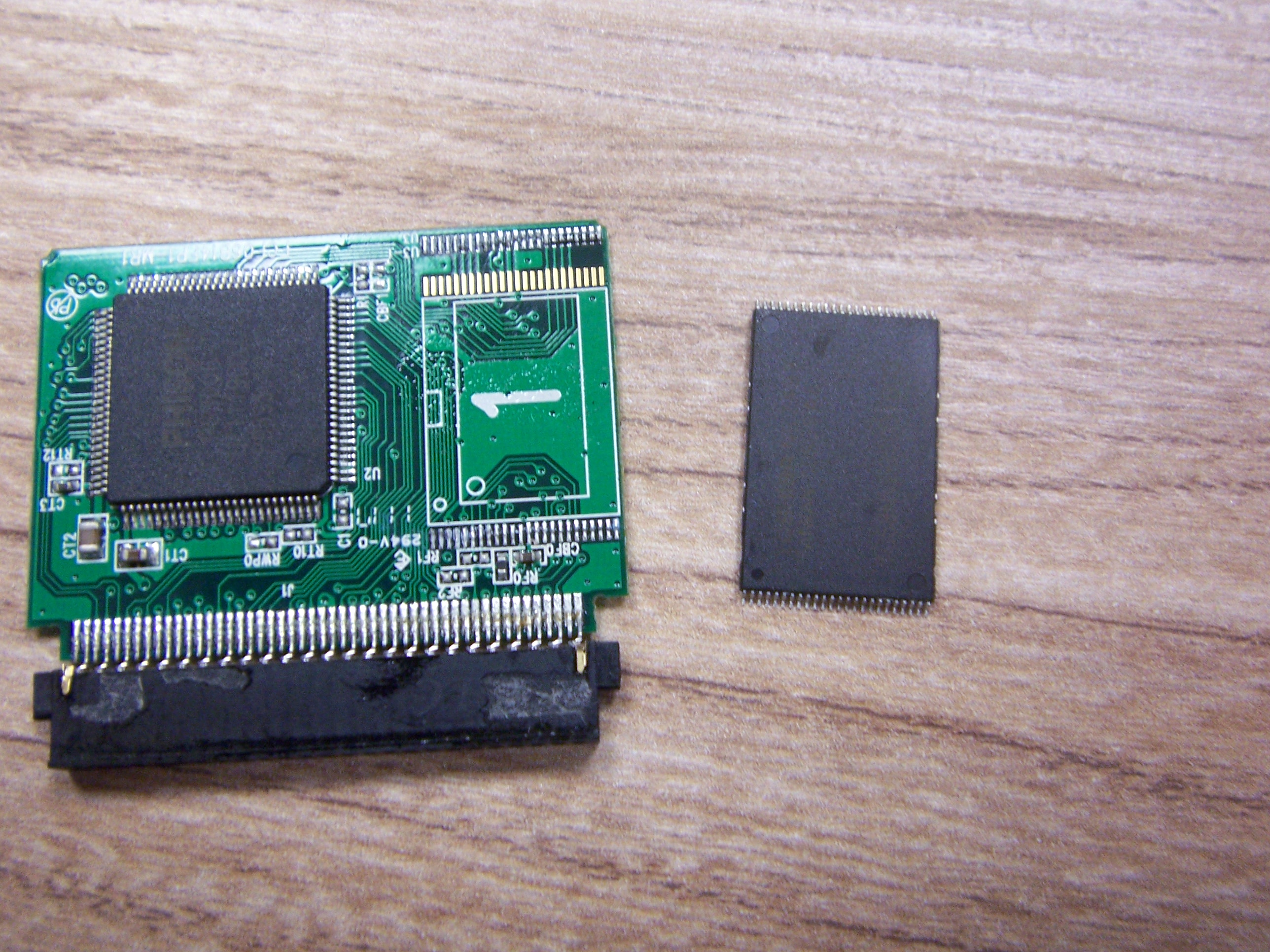 Odlutowany Chip NAND Flash obok płytki drukowanej karty CF, na płytce nadal przylutowany kontroler pamięci flash 