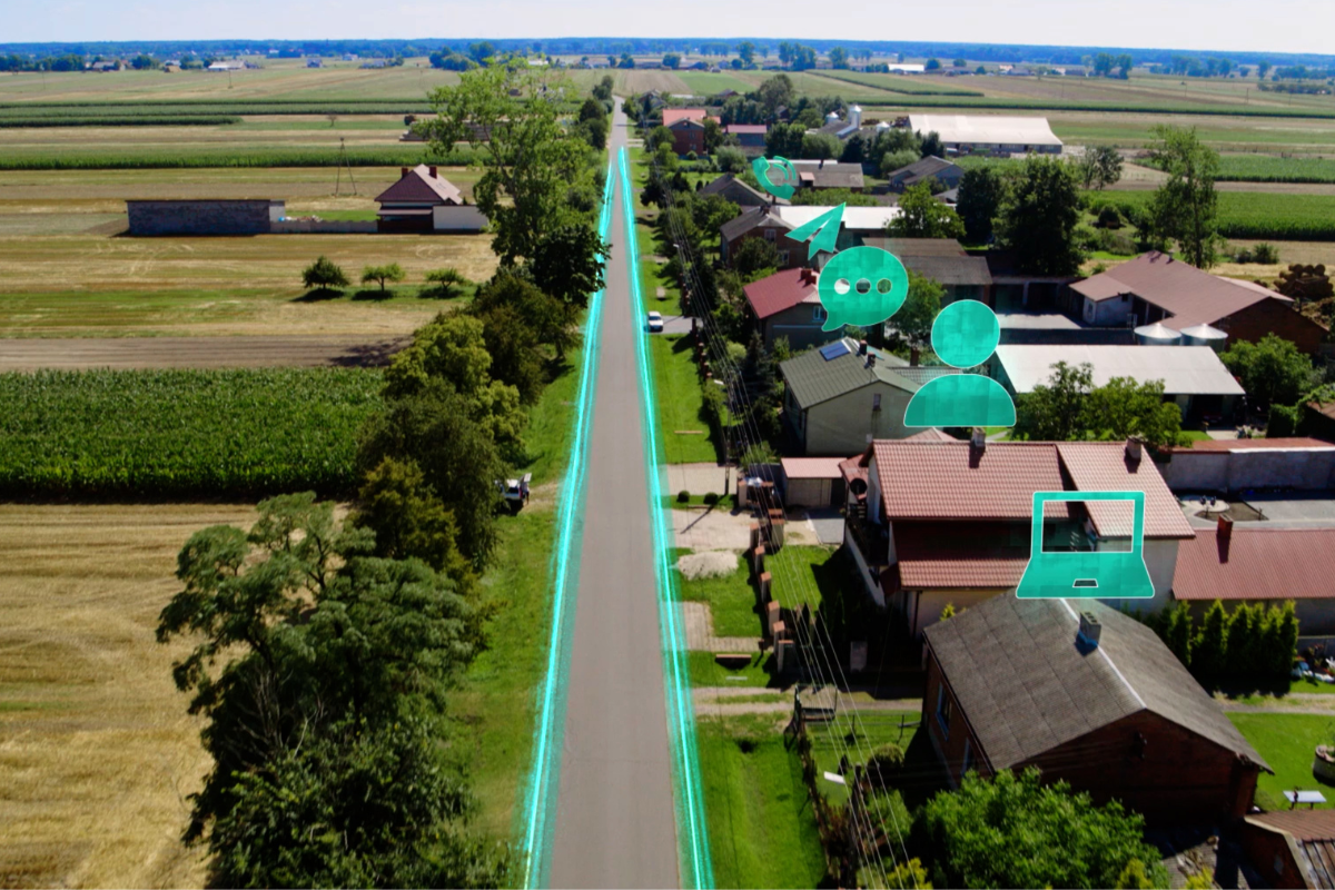 Panorama z widokiem na domki, pola i drogę wzdłuż której idzie światłowód