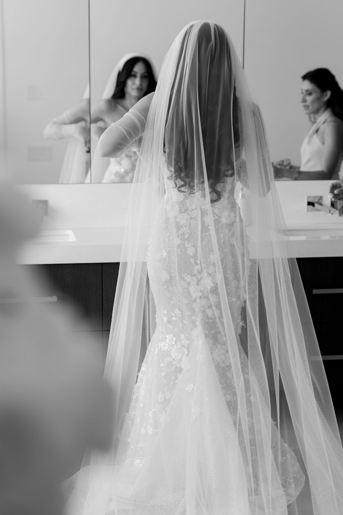 A bride with a long veil looking in the mirror getting ready on her wedding day photographed by torontos top wedding photographer Whitney heard.