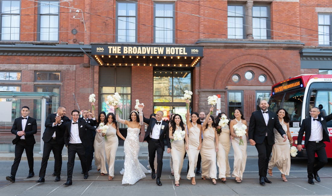 An energetic bridal party walking at the Broadview hotel with a TTC bus passing by/.
