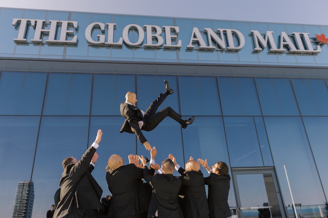 Groomsmen having fun tossing the groom in the air at a wedding in Toronto at the Globe and Mail Center.