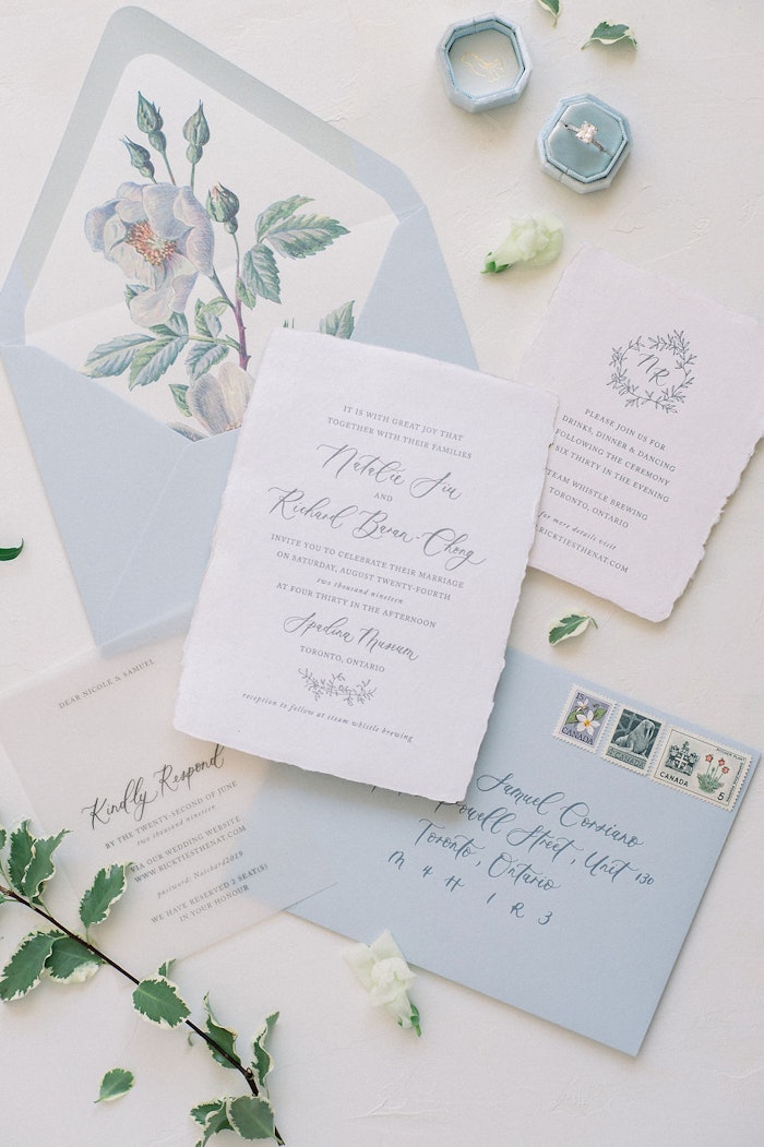 Toronto wedding photographer capturing soft blue wedding stationery flat lay with rings and perfume at Spadina House Museum