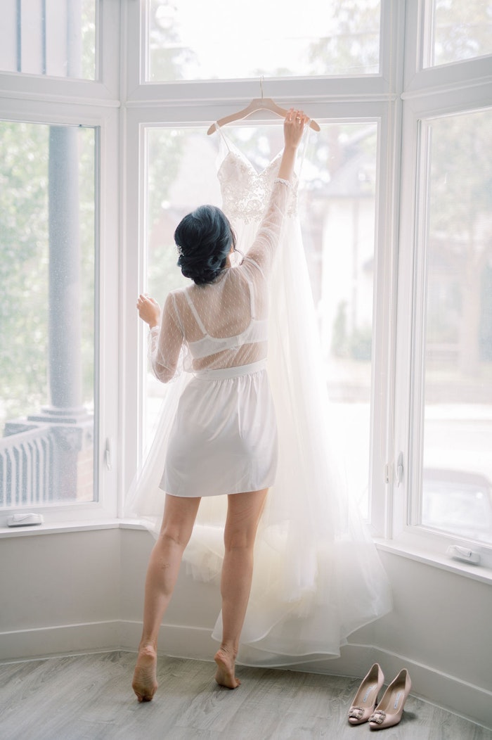 Bride hanging wedding dress in natural window light at Spadina House Museum Toronto wedding morning