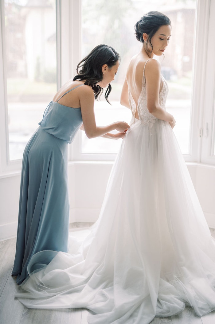 Bridesmaids helping bride into wedding dress with soft blue colour palette at Spadina House Museum Toronto