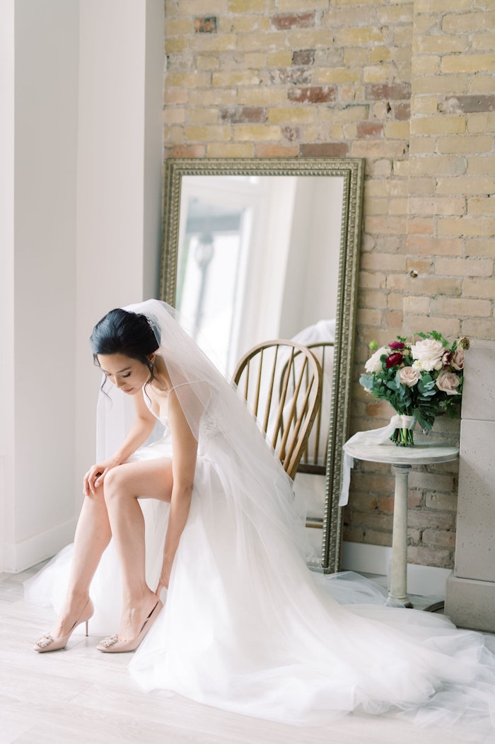 bride putting on her shoe in wedding dress with soft blue colour palette at Spadina House Museum Toronto