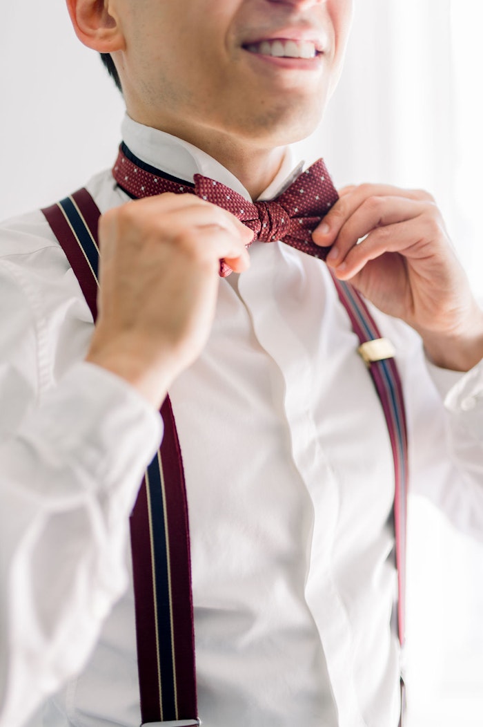 Groom putting on his red bow tie photographed by Whitney heard in Toronto