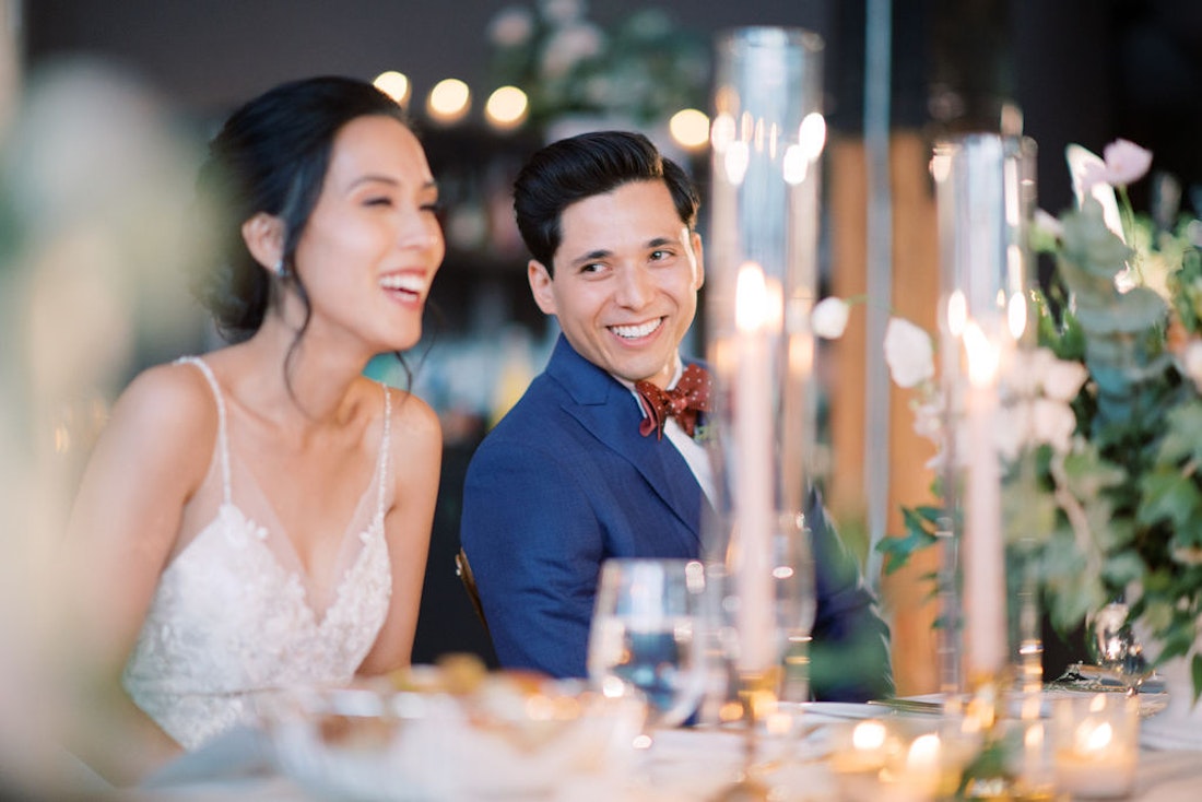 Groom enjoying the moment during his wedding reception and reacting to a speech by looking over to his bride.