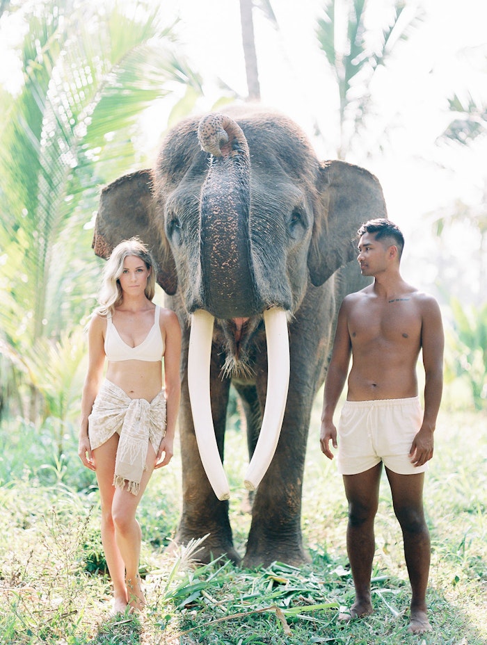 Couple standing with elephant in Bali during a romantic engagement session, captured in soft natural light with a cinematic editorial style
