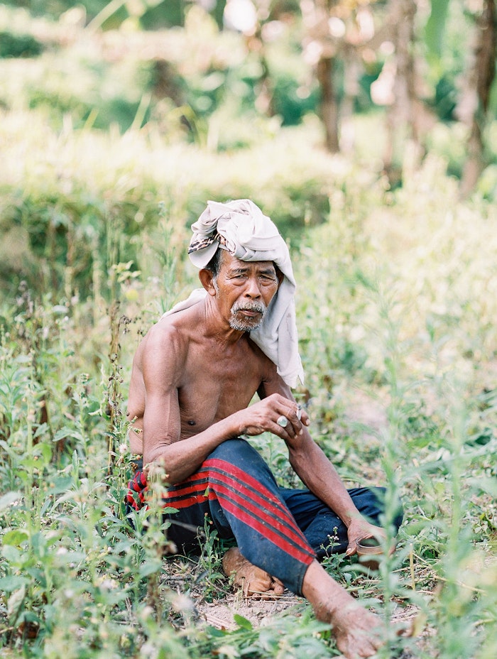 Portrait of a local man sitting in a field in Bali, captured in a documentary style with natural light and soft tones