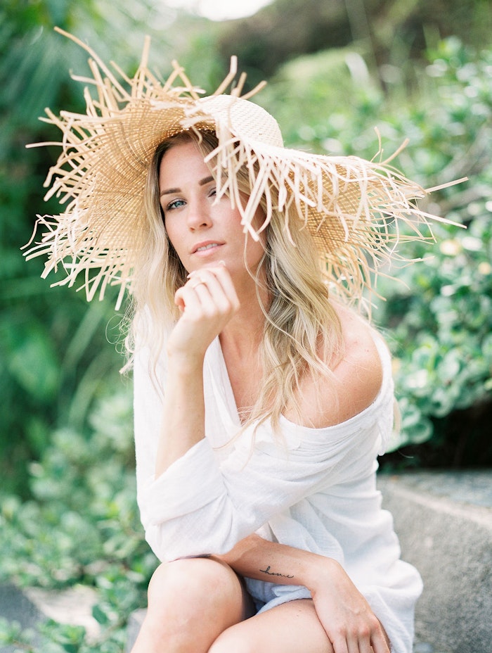 Bride wearing a straw hat in Bali, photographed in soft natural light with a romantic and editorial portrait style