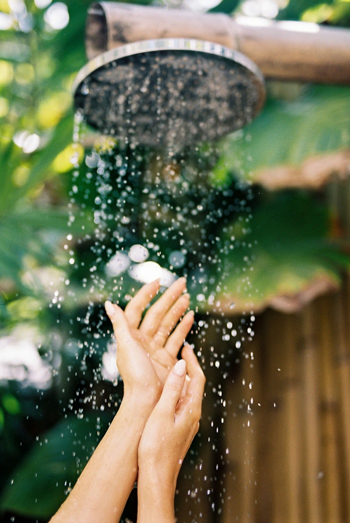 Close-up of hands under running water in Bali, captured with soft focus and artistic natural light detail