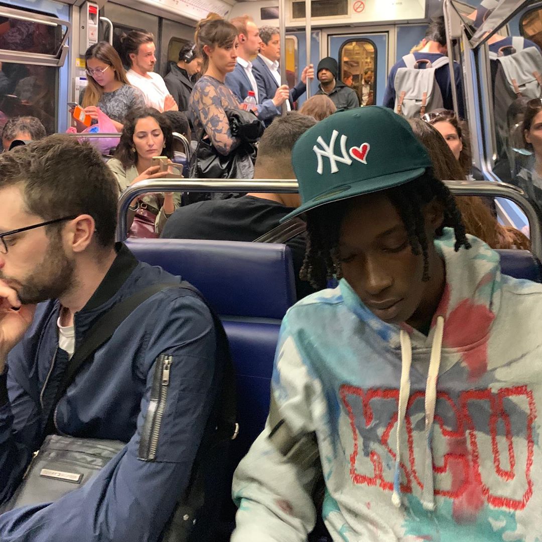 A man sitting in the subway wearing a gap sweater.