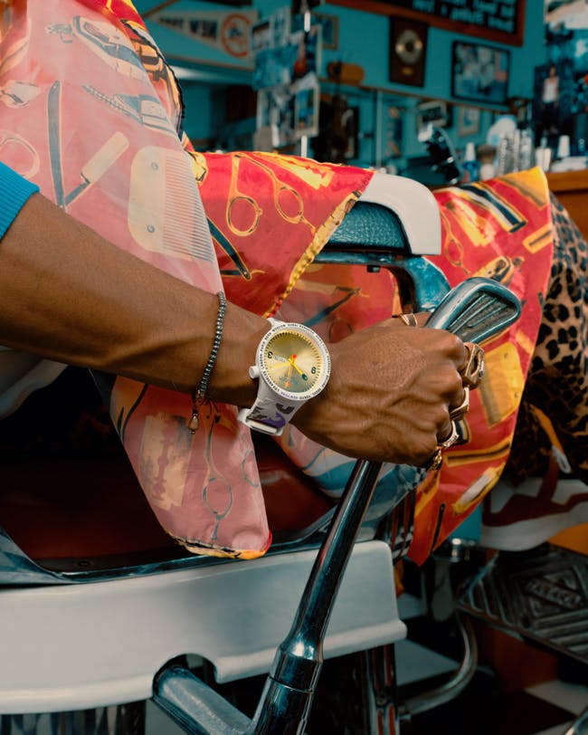 A man sitting on a chair with a swatch watch on his arm.