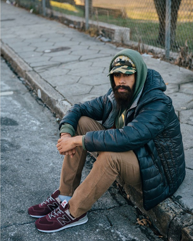 A man sitting on the sidewalk wearing new balance sneakers.