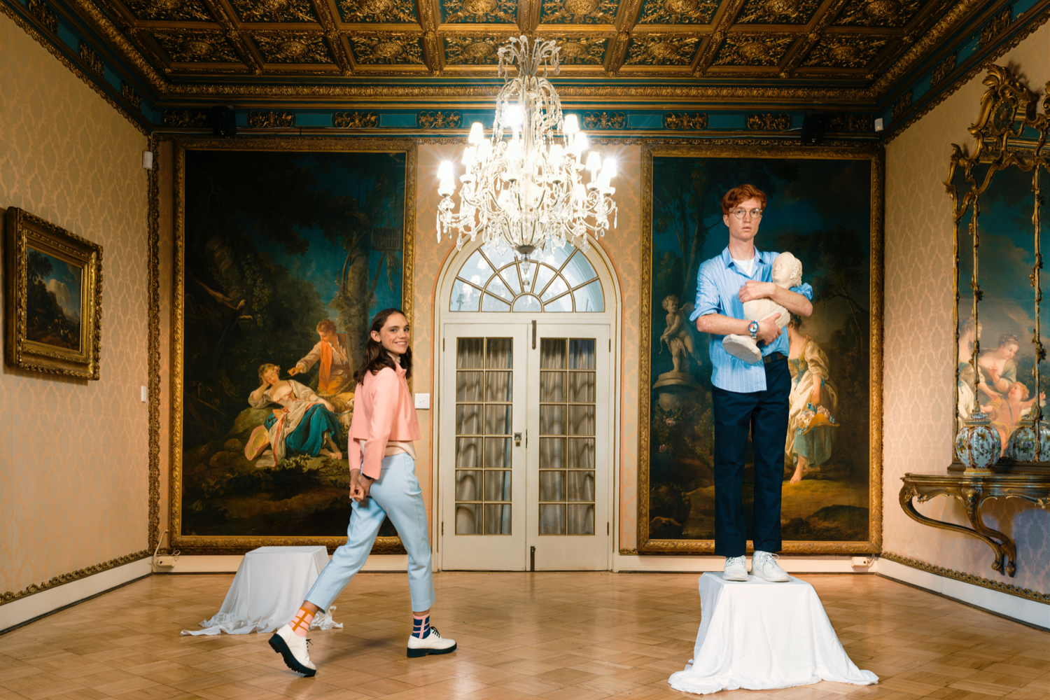 A man posing as a bust and a woman walking around the room.