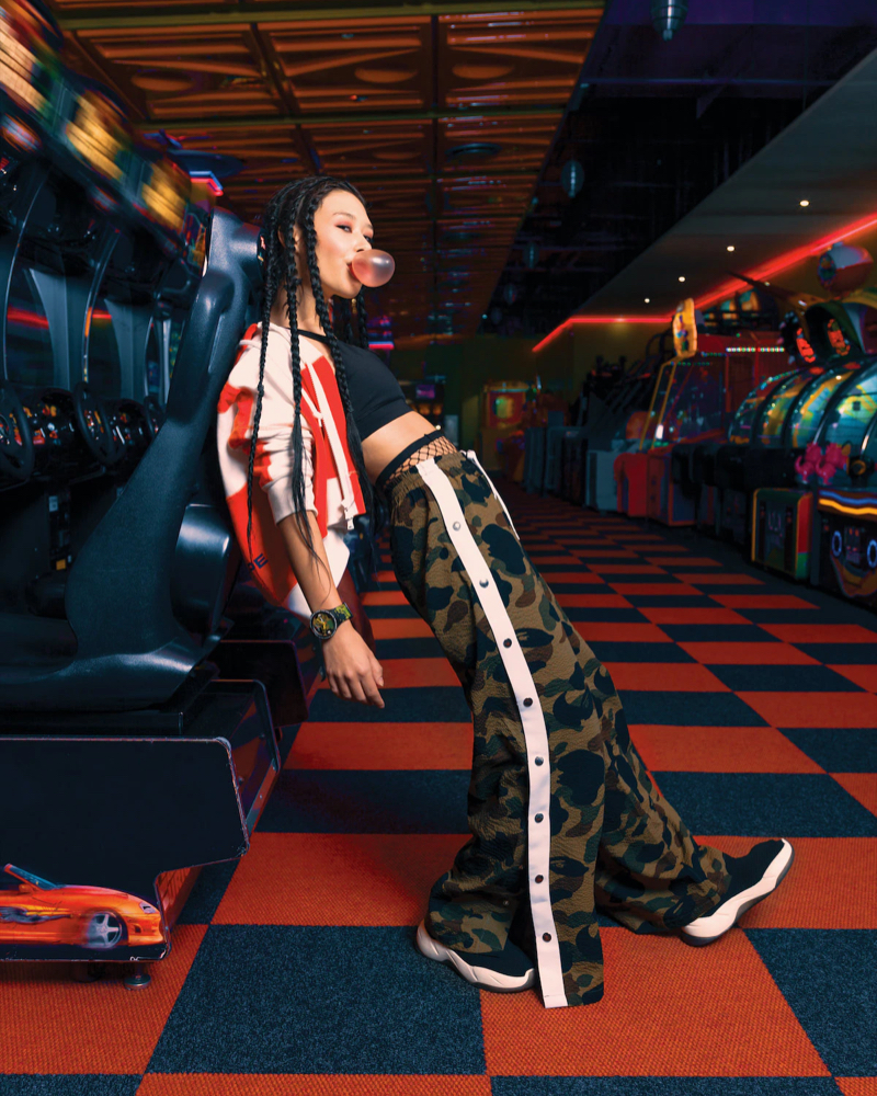 A woman posing in a arcade hall wearing a swatch x bape watch.