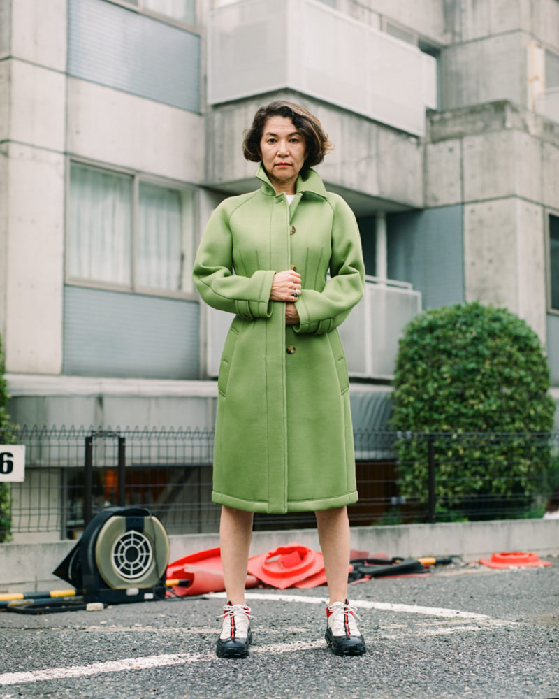 A woman standing on a parking lot in front of concrete building.