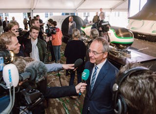 Minister Kamp wordt geïnterviewd tijdens de perspresentatie van de Delft Hyperloop. Op de achtergrond de ‘pod’.