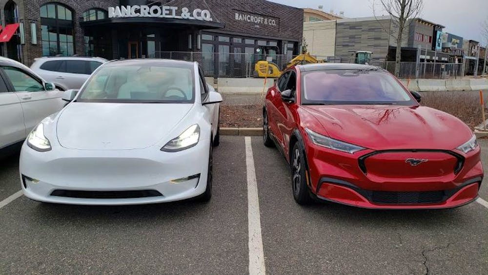 Beyaz Tesla Model Y'nin yanında Kırmızı Mustang Mach-E