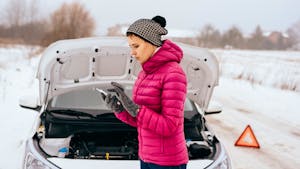 Woman in the middle of a snowy road with a broken car