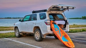 A kayak  being loaded into Toyota 4 Runner SUV on a lake shore at dusk after paddling session.