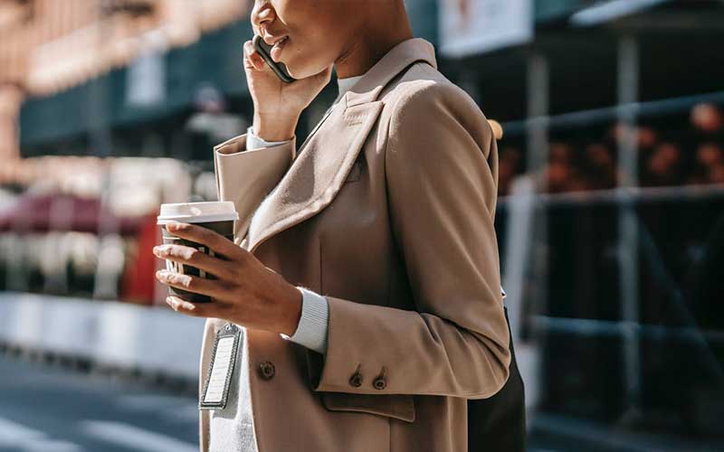 woman on the phone while holding a cup of takeout coffee
