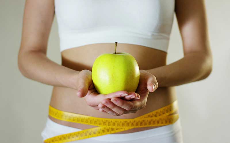 woman holding a green apple and a measuring tape around her waist