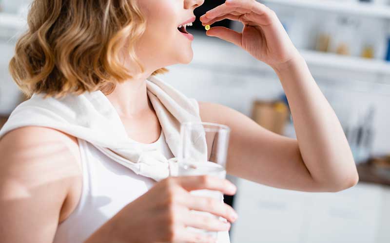 woman taking a pill while holding a glass of water