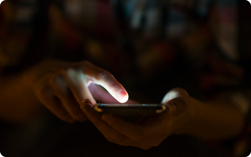 Woman holding mobile phone in dark room with screen lit up