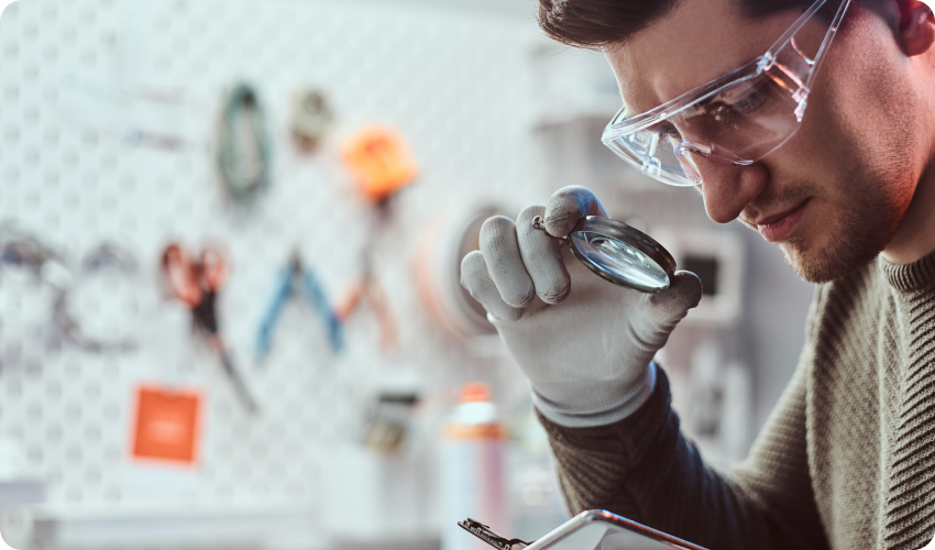 Technician uses magnifying glass to inspect a mobile phone