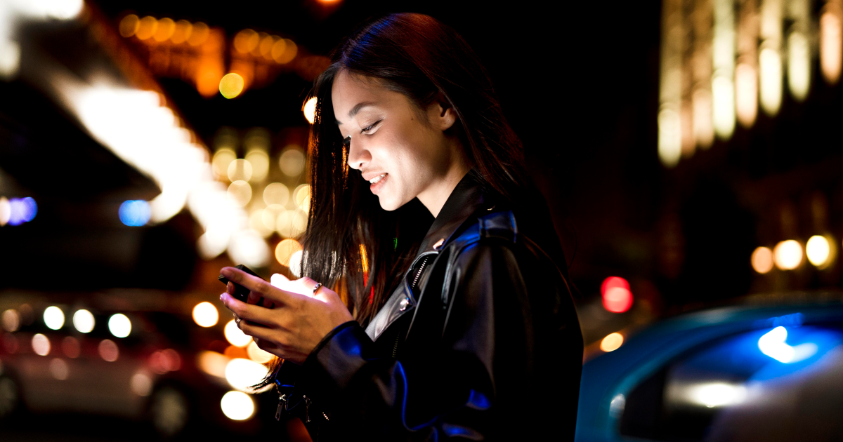 Woman using a phone at night in a lit up city