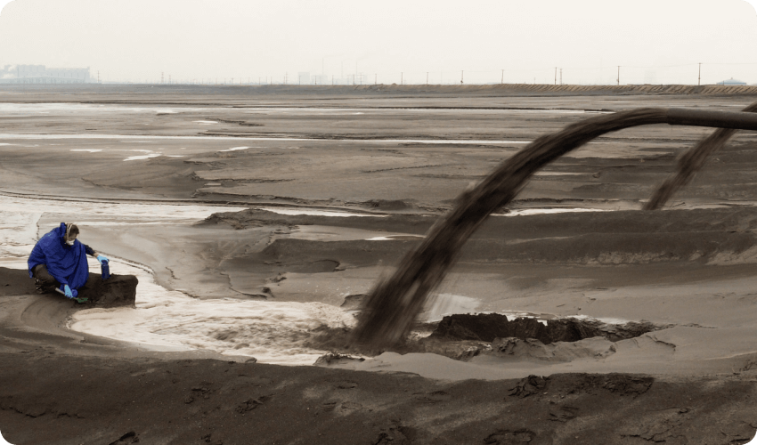 The Baotou river in Mongolia China showing a man collecting a sample of thick black liquid