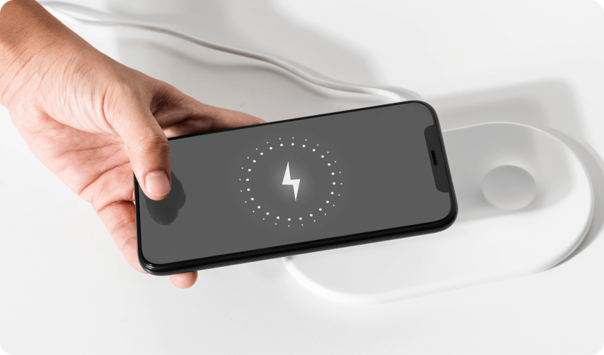 a male hand holding an iphone above a wired charging pad on white desk