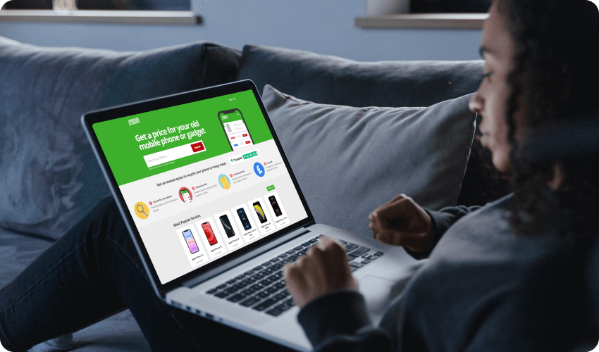 woman on a sofa browsing compare and recycle website on a laptop to sell a mobile phone