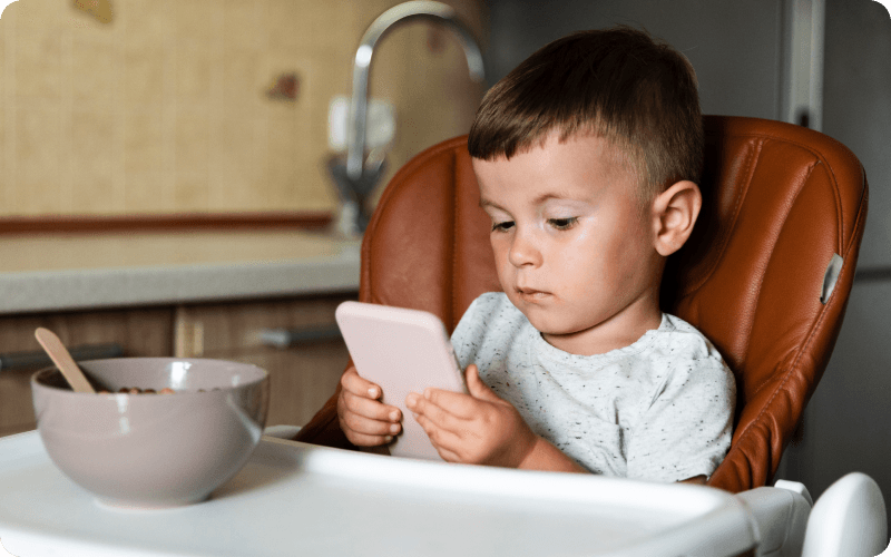 a boy holding a smartphone whilst having a meal