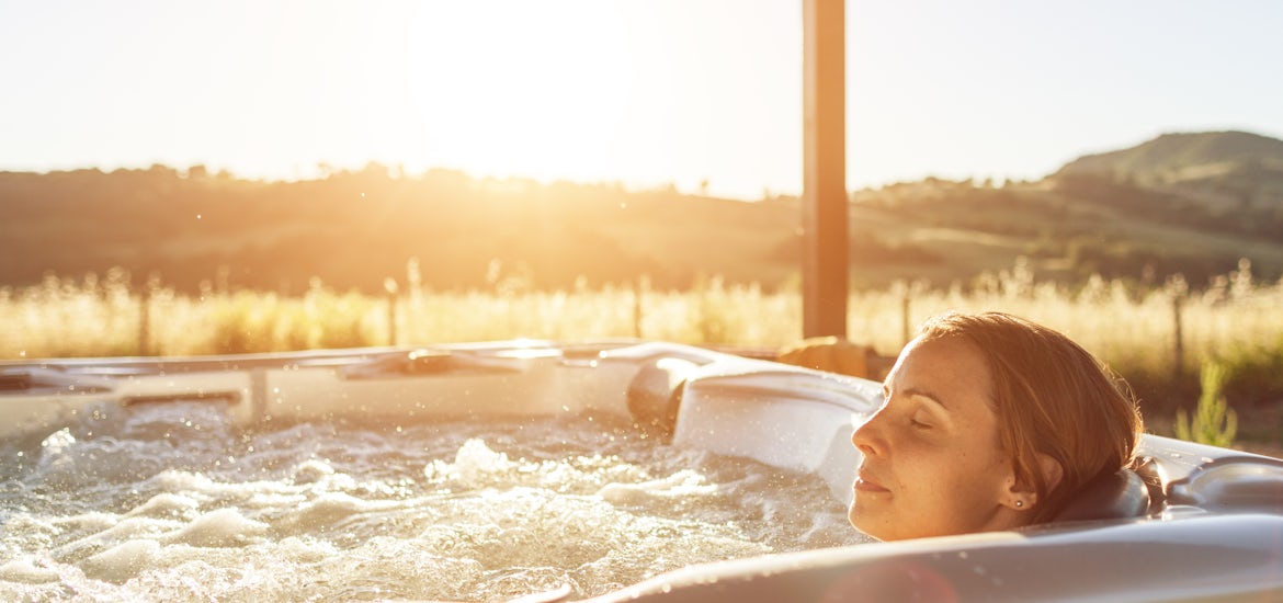 Woman reclining in a spa's back shiatsu seat, experiencing targeted hydrotherapy jets in a tranquil outdoor setting