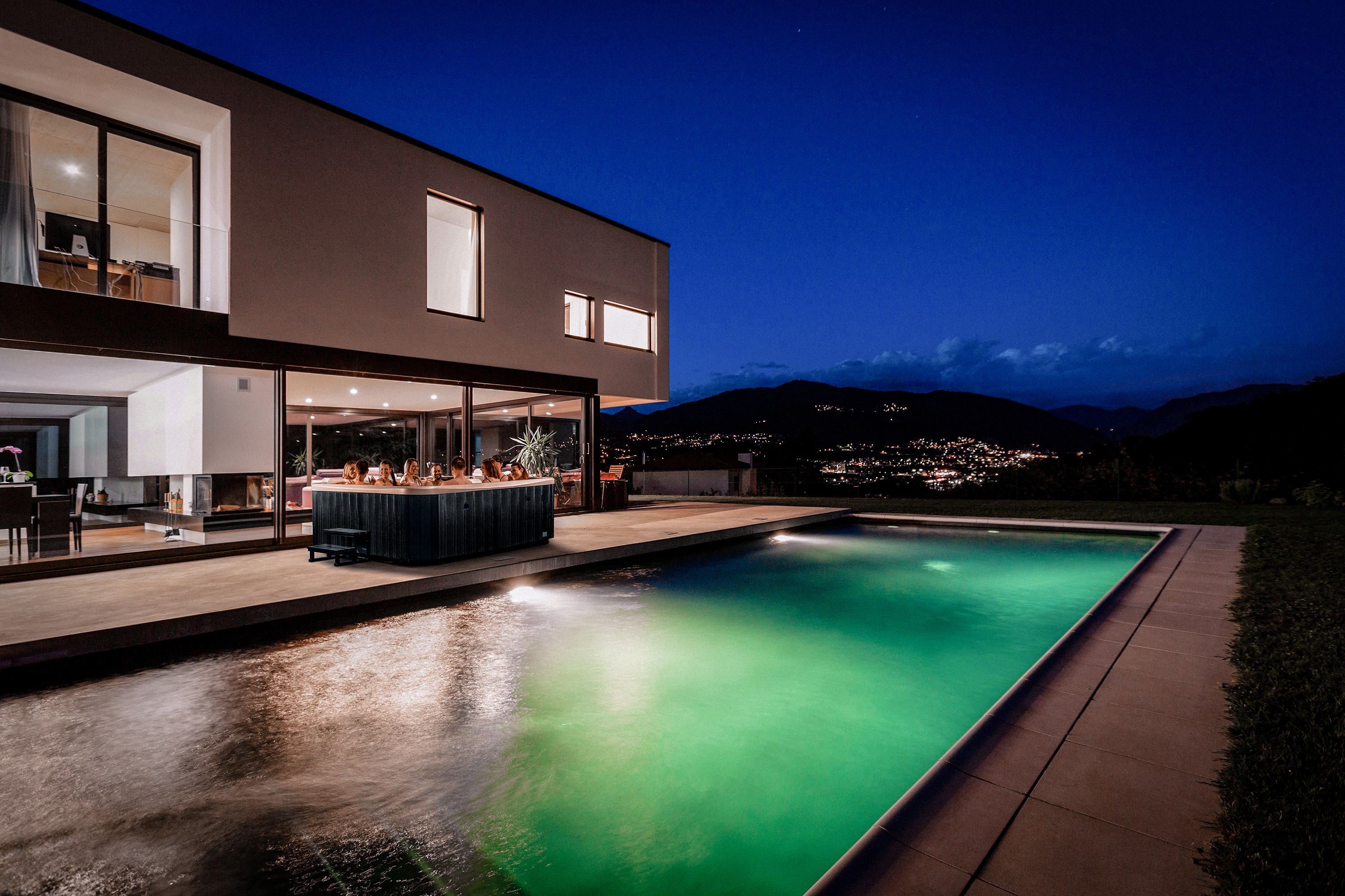A group of people relax in the Vortex Spas Titanium, enjoying hydrotherapy jets in a stylish outdoor setting with warm ambient lighting.