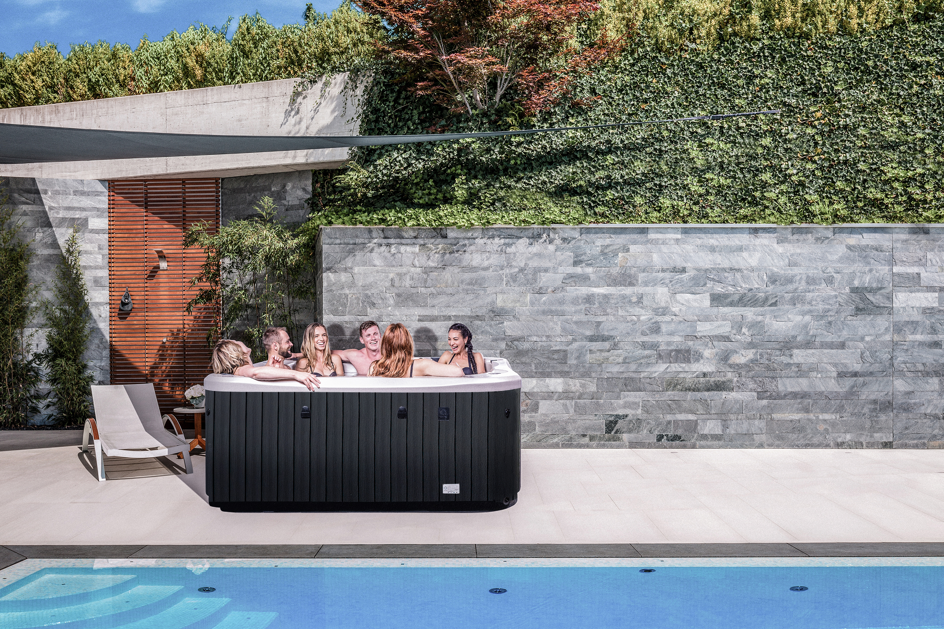Group of 6 friends enjoying on a Cobalt spa pool that is beside a large pool