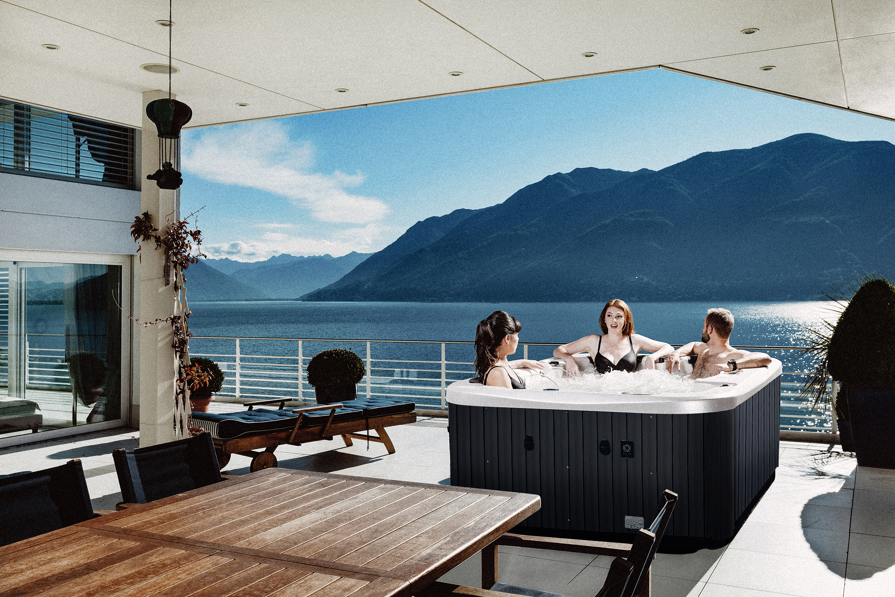 Three friends enjoying soaking on a Neon spa pool overlooking a scenic lake and mountain view