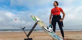 Foto van een man op het strand met een surfplank op de grond