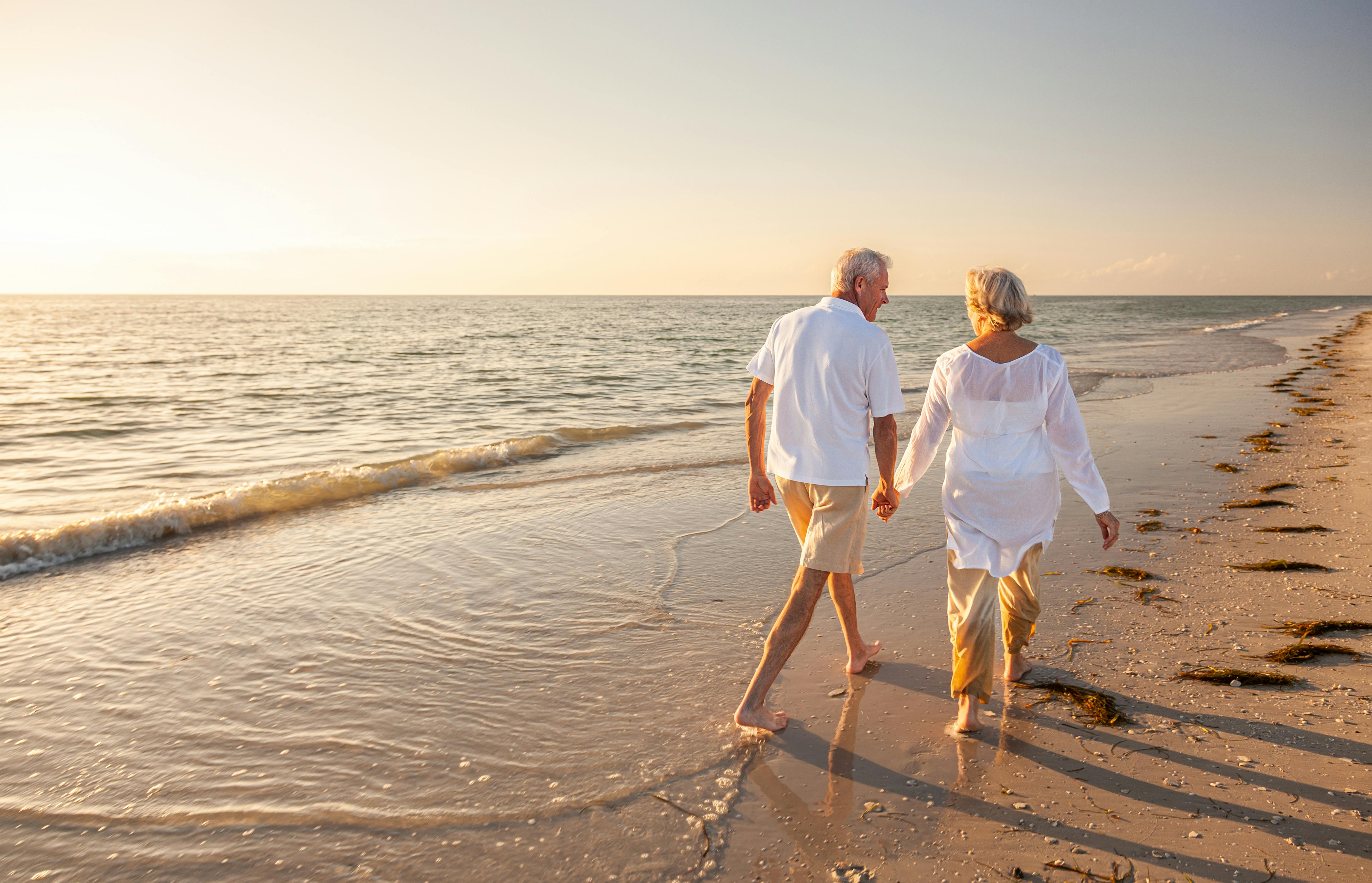 old retired couple walking and holding hands on a beach at sunset