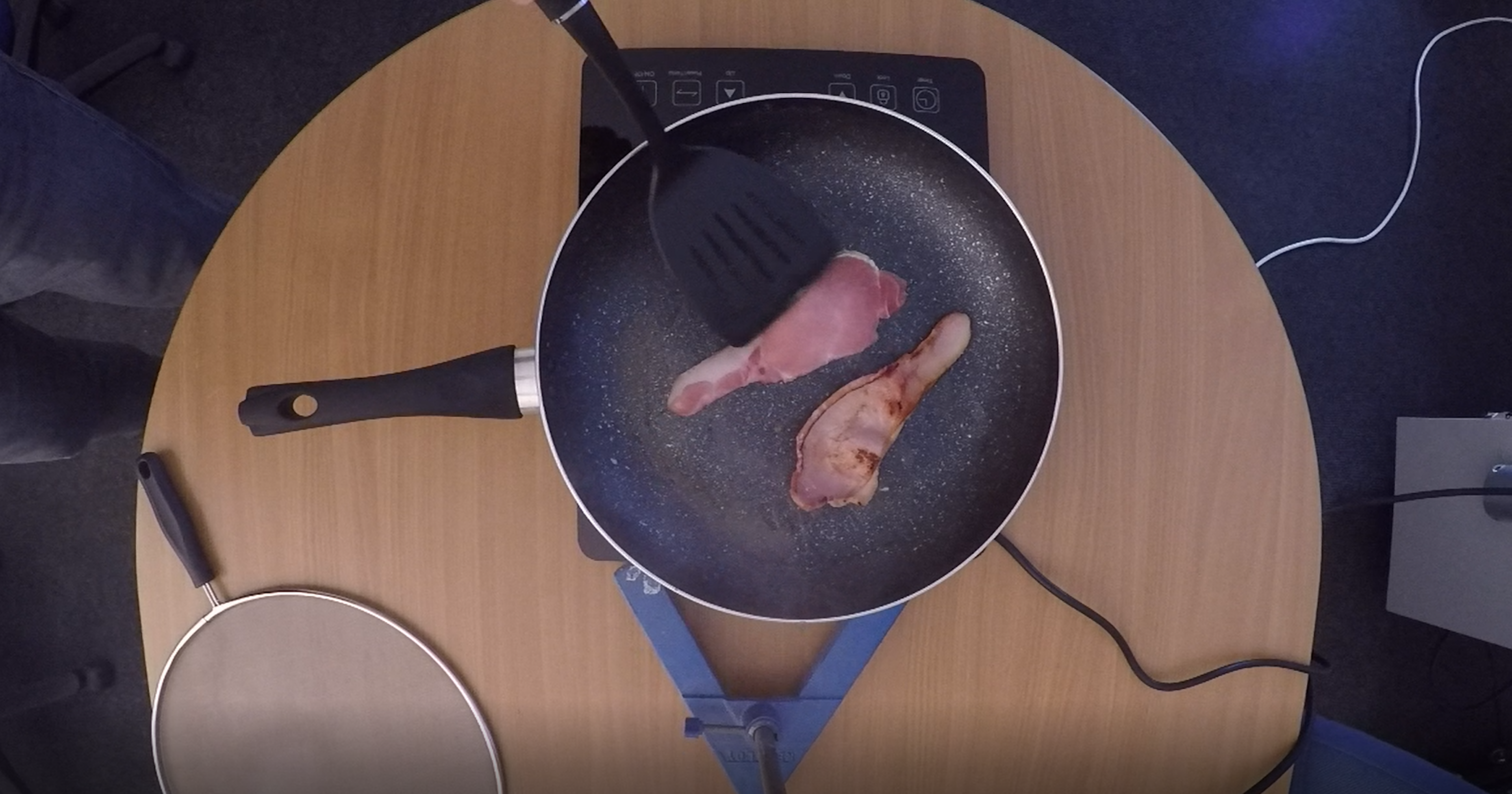 Bacon being turned in a pan to monitor emissions during cooking