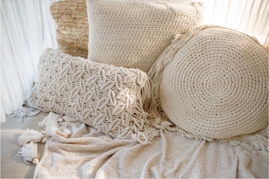 Almofadas de macramê branco e manta de tricô no sofá. 