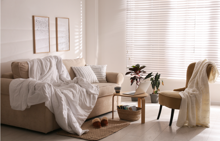 Sofá confortável bege com cobertor e uma poltrona com manta por cima em quarto elegante