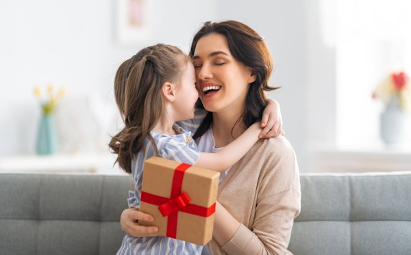 Criança abraça a mãe que segura uma caixa de presente na mão sorrindo