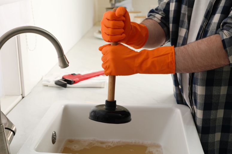 Homem segurando desentupidor em uma pia entupida