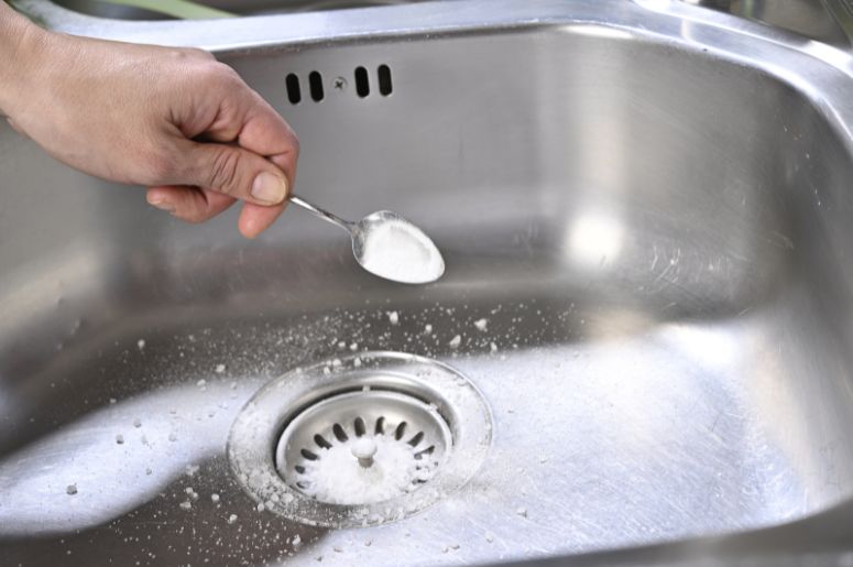 Pessoa jogando soda c&aacute;ustica na pia da cozinha