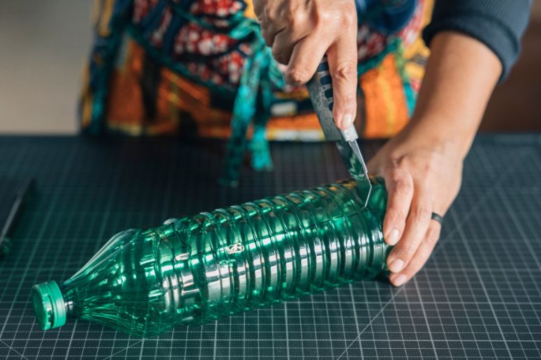 Mulher cortando o fundo de uma garrafa PET